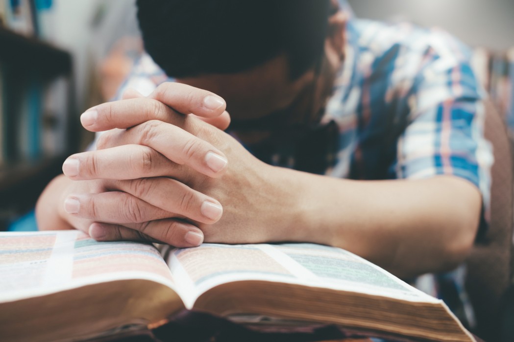 Hands clasped in prayer over an open Bible