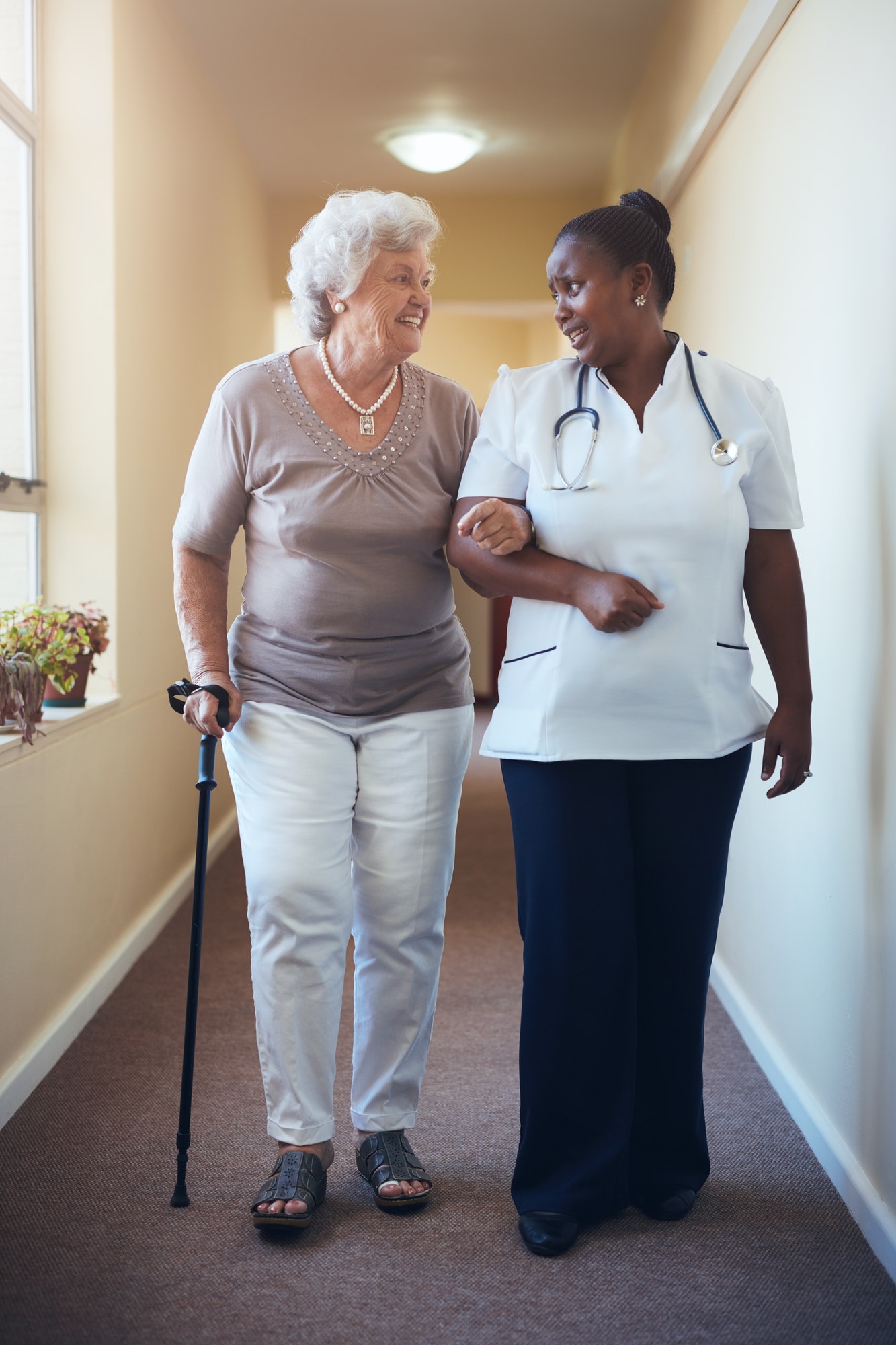 Senior woman walking being helped by female nurse