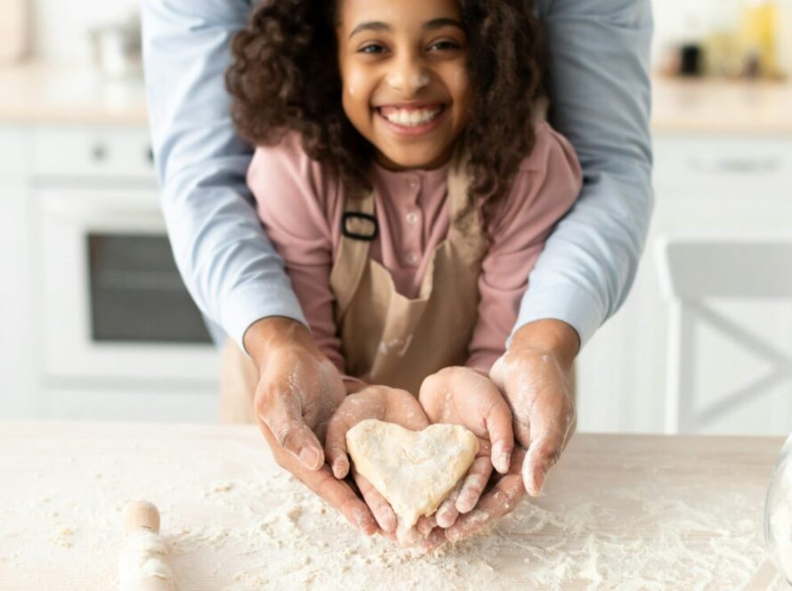 Happy black man and girl holding dough in heart shape